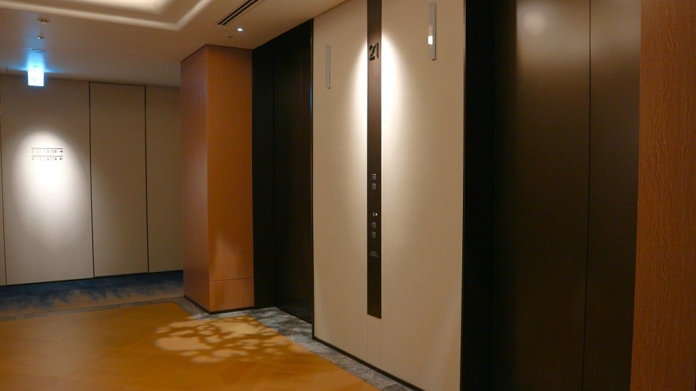 波をイメージした廊下と木漏れ日のダウンライトが光るエレベーターホール